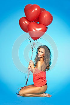 Happy pretty woman holding bunch of red air balloons at the studio