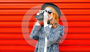 Happy pretty woman holds retro camera on red background
