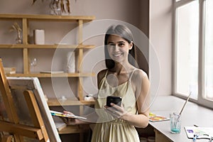 Happy pretty young artist holding cellphone craft professional portrait