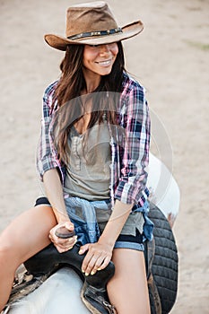 Happy pretty young woman cowgirl riding a horse outdoors