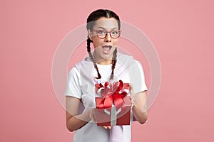 Happy pretty young woman holding gift box on pink background, blank copy space for your advertising content