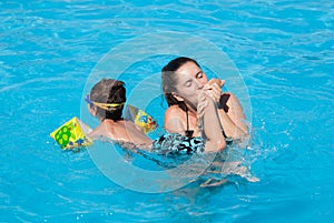 Happy pretty young woman mother kissing her swimming little child foot with love in blue fresh water summer outdoor pool