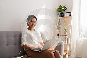 Happy pretty young woman sitting on sofa and using laptop at home