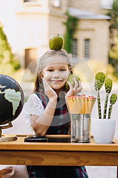 Happy Primary Girl Sit At Desk Hold Apple on Head