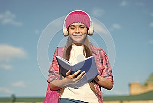 Happy primary school kid read book listening to foreign language course playing in headphones sunny outdoors, english