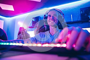 Happy professional cyber sport gamer playing online computer game with headphones, Blurred Red and Blue background