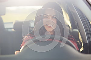 Happy professional female driver looks through windshiled, drives car, being in good mood as there is no traffic jam on road, has