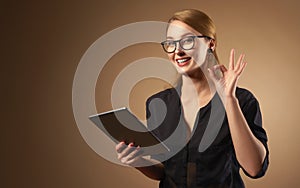 Happy professional girl wearing glasses and holding tablet isolated on brown background