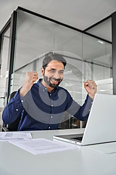 Happy professional Indian business man celebrating win using laptop at work.