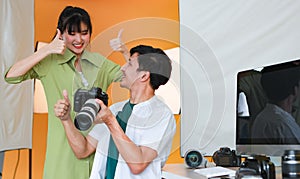 Happy professional male photographer holding DSLR camera smiling while showing pictures on camera screen to pretty young model who