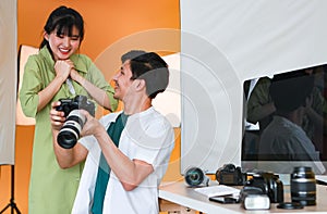 Happy professional male photographer holding DSLR camera smiling while showing pictures on camera screen to pretty young model who