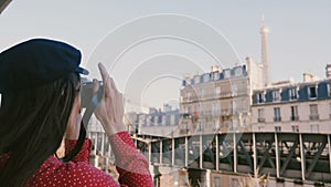 Happy professional photographer woman in red dress taking a photo of the Eiffel Tower view in Paris with vintage camera.