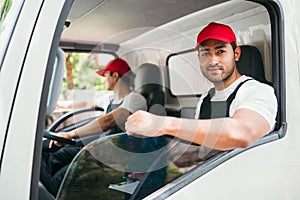 Happy professional truck driver with his assistant wearing a red cap, smiling and looking at the camera from a truck window.