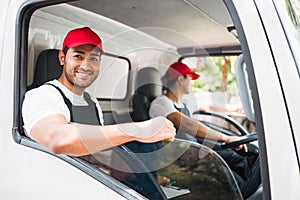 Happy professional truck driver with his assistant wearing a red cap, smiling and looking at the camera from a truck window.