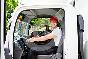 Happy professional truck driver with his assistant wearing a red cap, smiling, looking at the camera from a truck window.