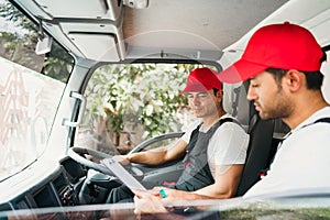 Happy professional truck driver with his assistant wearing a red cap smiling and talking about the parcel with checklists.
