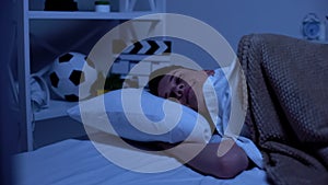 Happy promising boy lying in bed in evening, time for relaxation, healthy sleep photo