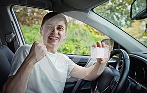 Happy and proud guy showing his driver license out of the car window, keeps fist up tight as a winner celebrating victory. Passing