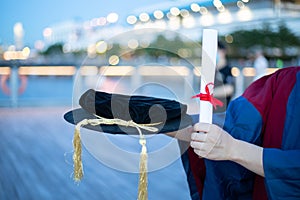 Happy proud PhD graduated male student in Academic dress gown holds Graduation cap or hat and diploma or certificate. Blurred