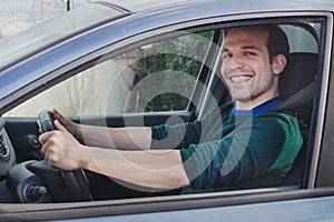 Happy proud young man driving car, smiling and looking to camera