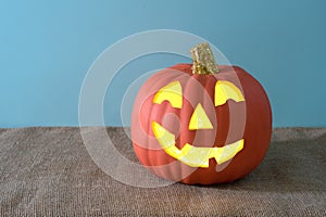 Happy Pumpkin for Halloween, carved and lighted, that`s on a burlap table with blue background with room or space for copy, text