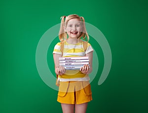 Happy pupil with backpack isolated on green with schoolbooks