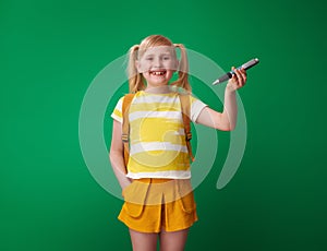 Happy pupil showing big pen isolated on green background