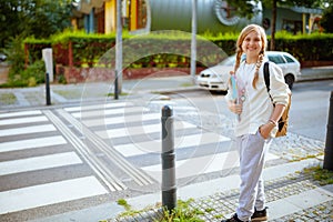 Happy pupil in sweatshirt crossing crosswalk outdoors in city