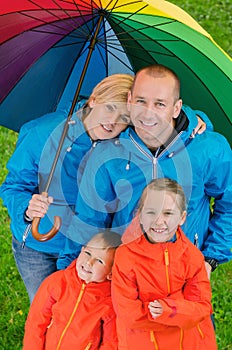 Happy rain family under colorful umbrella