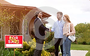 Cheerful realtor shaking hands with clients in front of residential building outdoors, free space