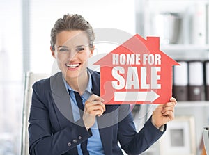 Happy realtor woman showing home for sale sign photo