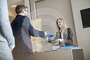 Happy receptionist giving file to businessman at convention center