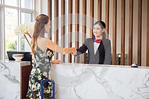 Happy receptionist and guest making handshake at hotel reception, receptionist standing at hotel counter with young female