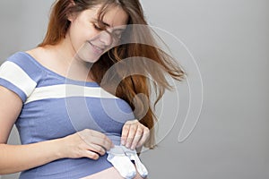 Happy red-haired pregnant woman holding little baby socks on belly on isolated grey background