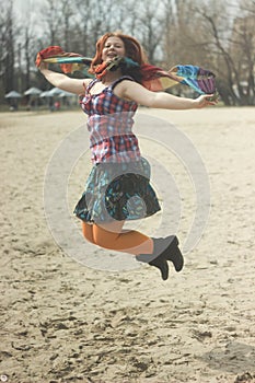 Happy red-haired young girl in bright hippie clothes in orange tights posing and laughing happily whirling and jumping