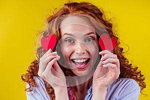 Happy redhead ginger curly girl businesswoman in a cotton shirt model hold decorative hearts Valentines Day gift on