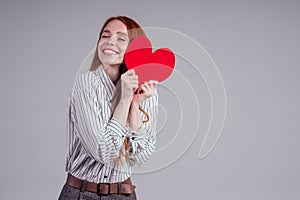 Happy redhead girl businesswoman in a striped shirt model sending air kiss with decorative hearts Valentines Day gift on