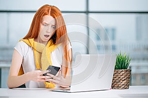 Happy redhead girl send an sms message to friend while working at modern office