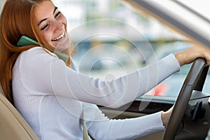 Happy redhead girl talking on her mobile phone behind the wheel driving a car