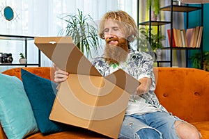 Happy redhead man shopper unpacking cardboard box delivery parcel online shopping purchase at home