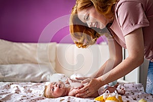 Happy redhead mother hugging little newborn baby lying together on cotton bed enjoying motherhood