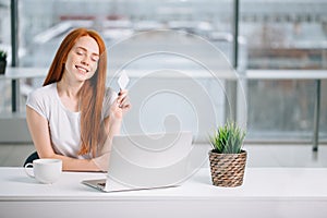 Happy redhead shopper deciding what to buy on line holding a credit card sitting