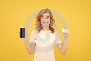 happy redhead woman showing credit or debit card and smartphone to make online shopping, buy online