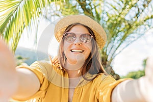 Happy redhead woman in straw hat take a selfie at vacation on a tropical island, palm trees in the background. Solo