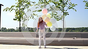 Happy redhead young woman carefree playing and jumping with large fountain of colorful balloons.