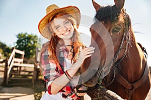 Happy redhead young woman cowgirl in hat with her horse