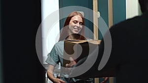Happy redhead young woman receiving parcel at home from delivery man on doorstep at apartment.
