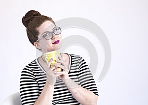 Happy redheaded woman loves her coffee and hold the cup close to her face with a smile in the studio on a white background