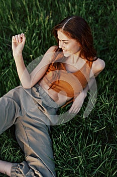 Happy redheaded woman sitting on fresh spring green grass in the garden smiling and looking out into the sun, view from