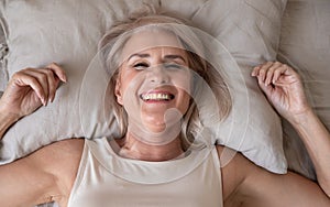 Happy refreshed elderly female lying in bed looking at camera